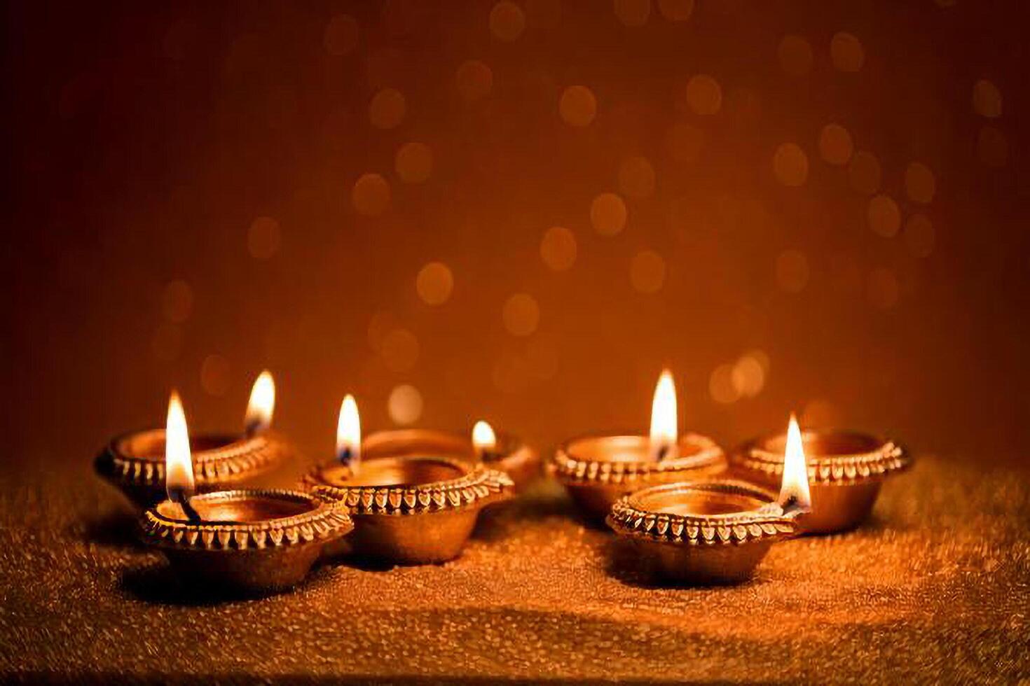 Four lit diya candles on a table with bokeh photo