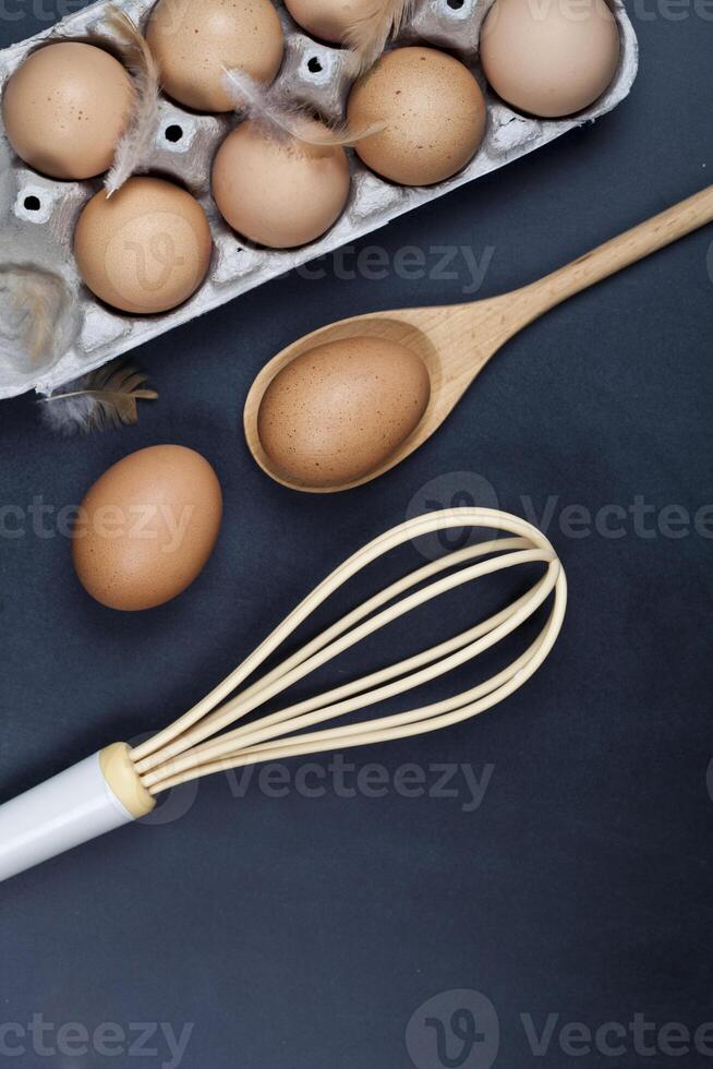 Eggs, wooden spoon, whisker and feathers. Kitchen utensil for cake, pastry or cookies on backboard background. photo
