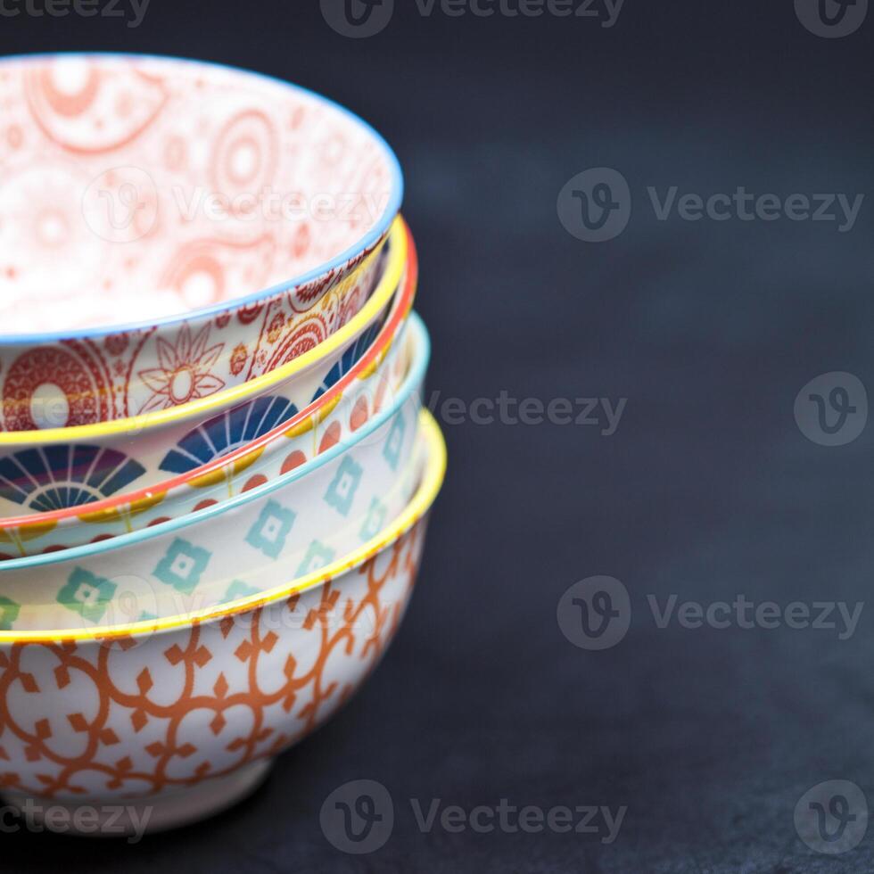 Stack of colorful empty ceramic bowls closeup on black board background. photo