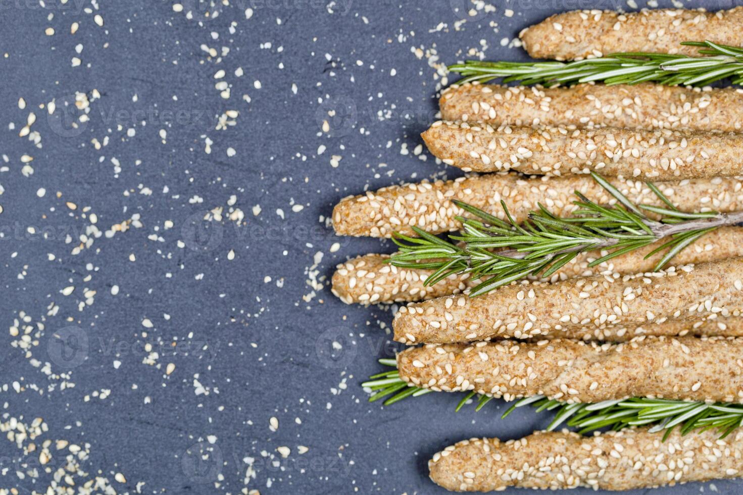 Italian grissini bread sticks with sesame and rosemary herb on black board background. photo
