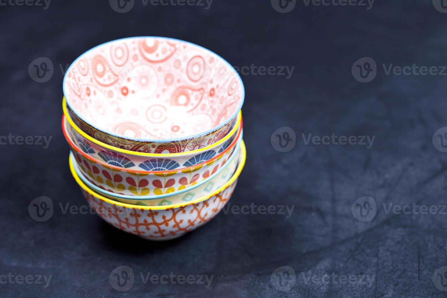 Stack of colorful empty ceramic bowls closeup on black board background. photo