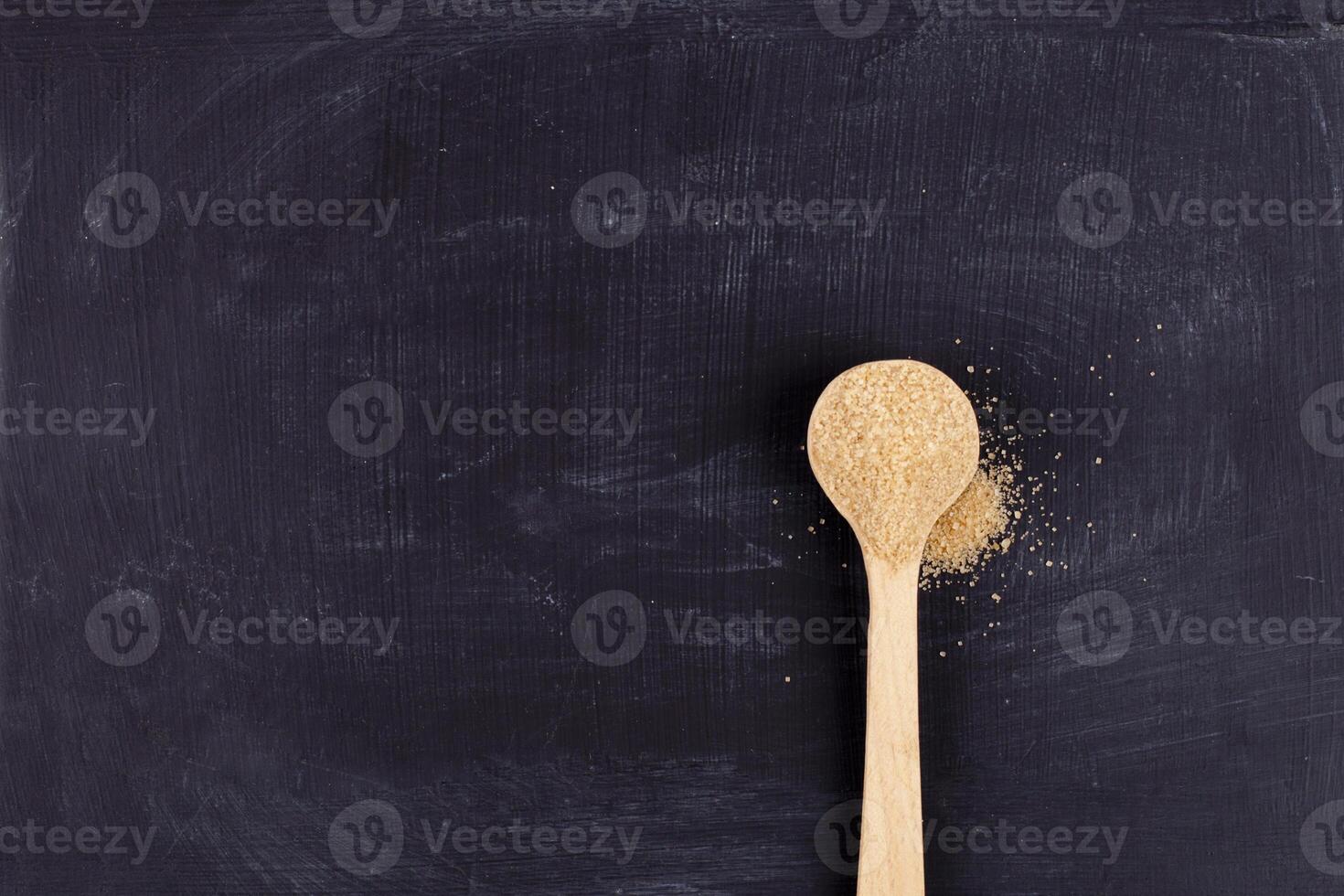 Brown cane sugar in wooden spoon on black background. photo