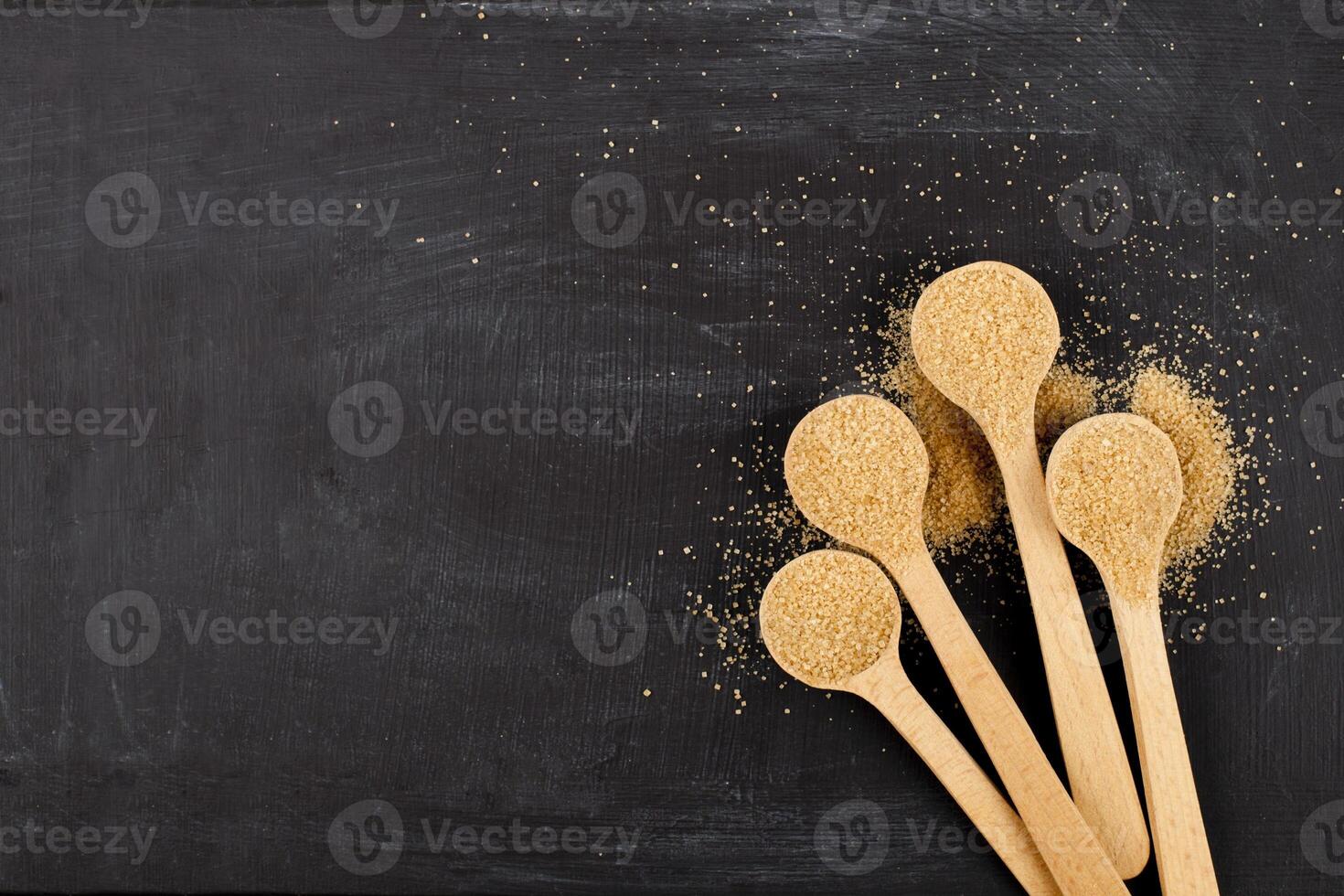 Brown cane sugar in four wooden spoons on black background. photo