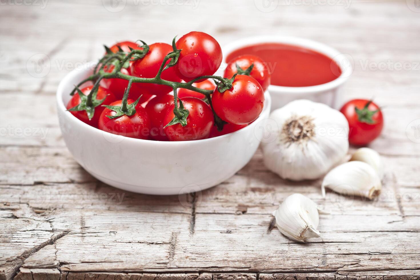 Fresh tomatoes in white bowl, sauce and raw garlic on rustic wooden table. photo