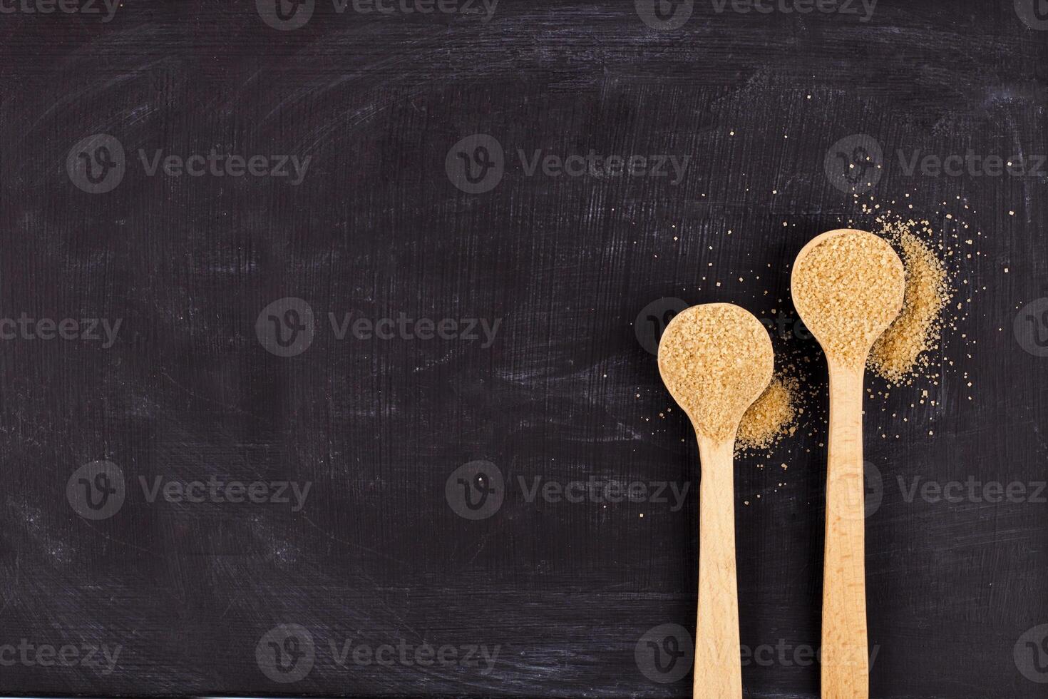 Brown cane sugar in two wooden spoons on black background. photo