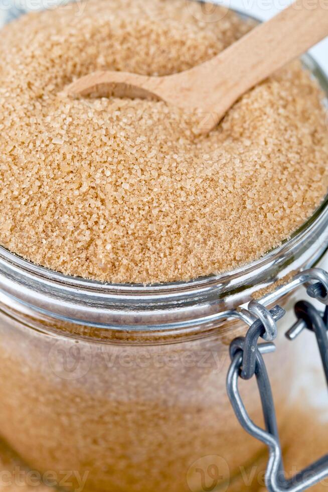 Brown cane sugar in glass jar and wooden spoon closeup image. photo