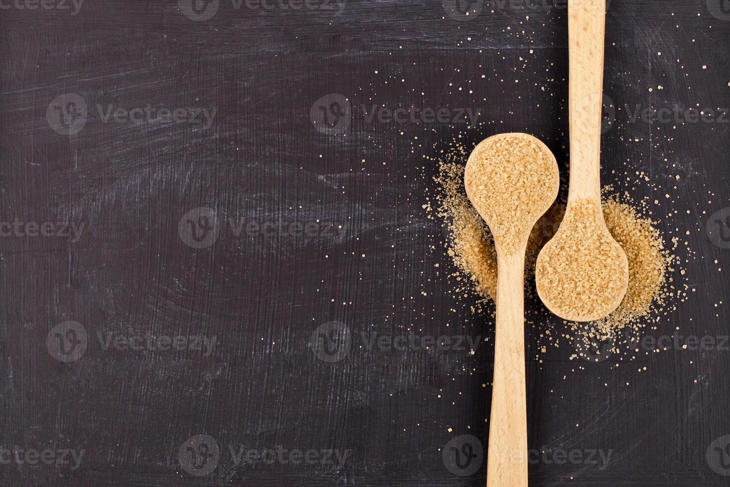 Brown cane sugar in two wooden spoons on black background. photo