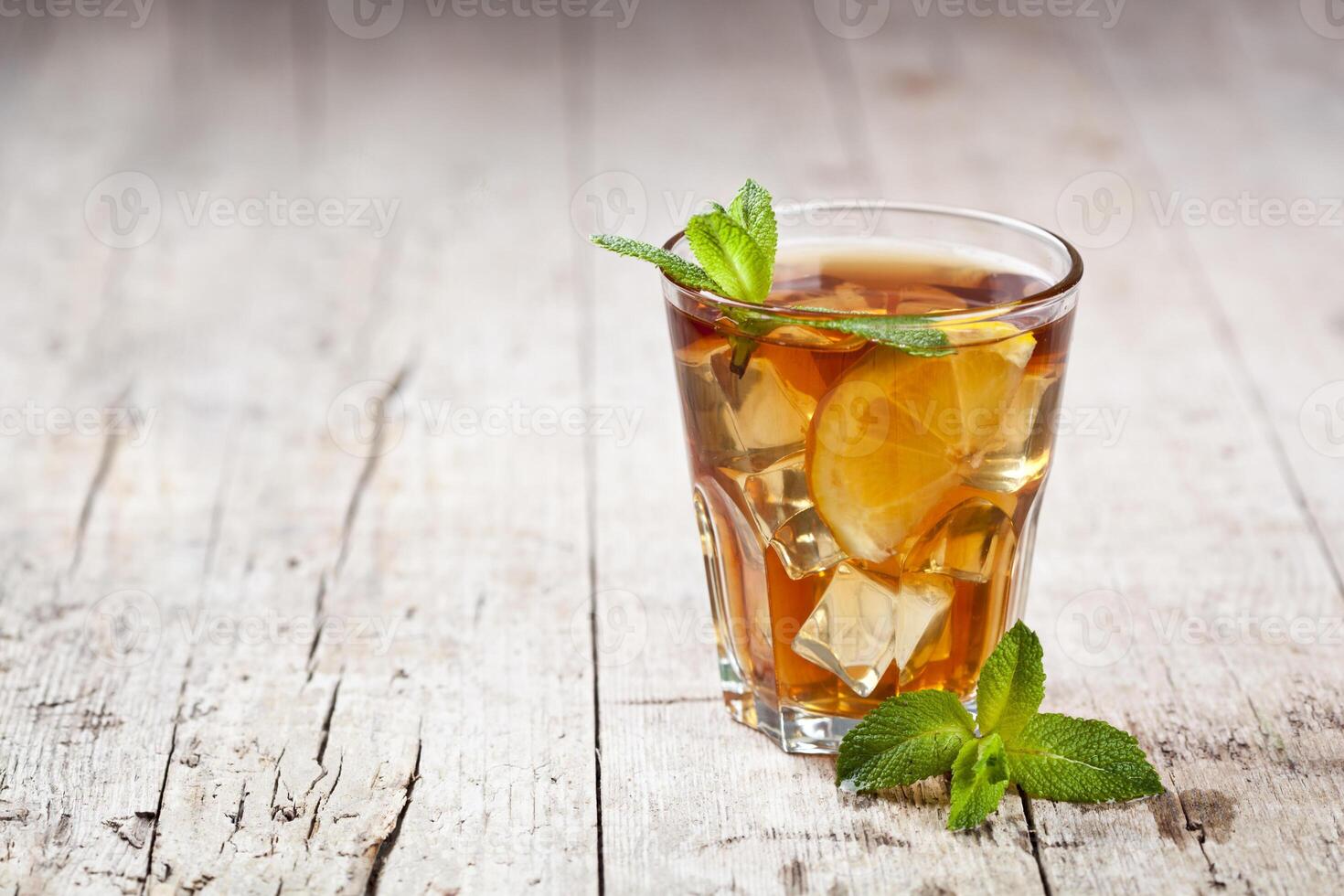Traditional iced tea with lemon, mint leaves and ice in glass on rustic wooden table background. photo