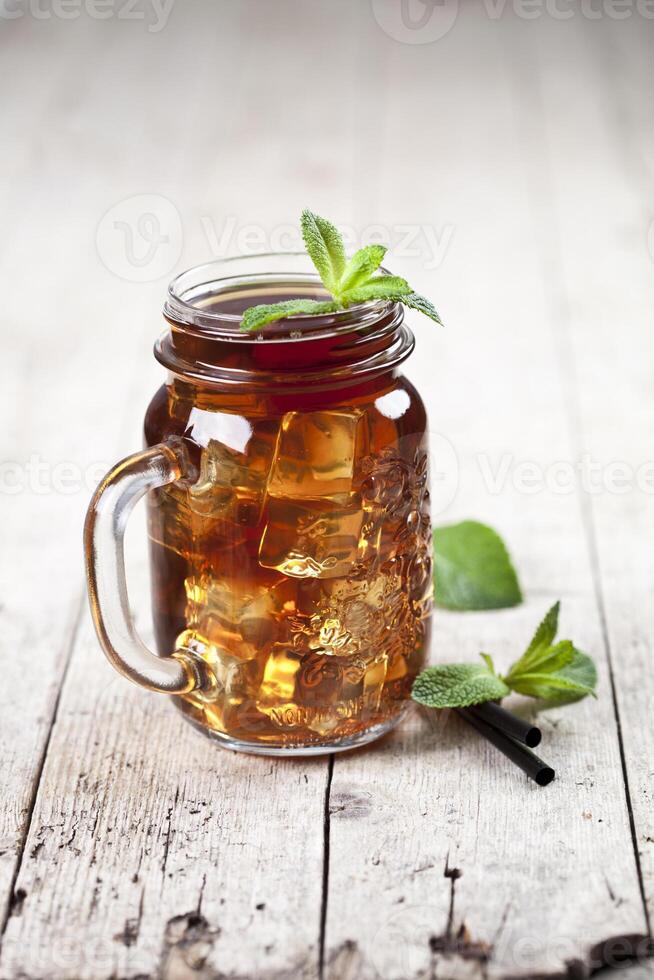 Traditional iced tea with lemon, mint leaves and ice cubes in glass jar on rustic wooden table photo