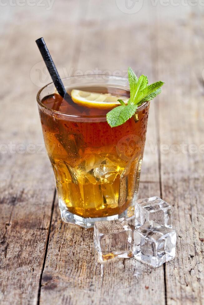 Traditional iced tea with lemon, mint leaves and ice cubes in glass on rustic wooden table. photo