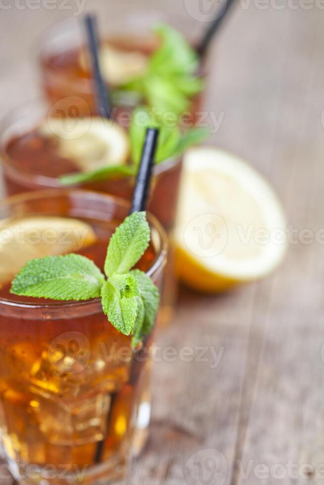 Traditional iced tea with lemon, mint leaves and ice cubes in glasses on rustic wooden table background. photo