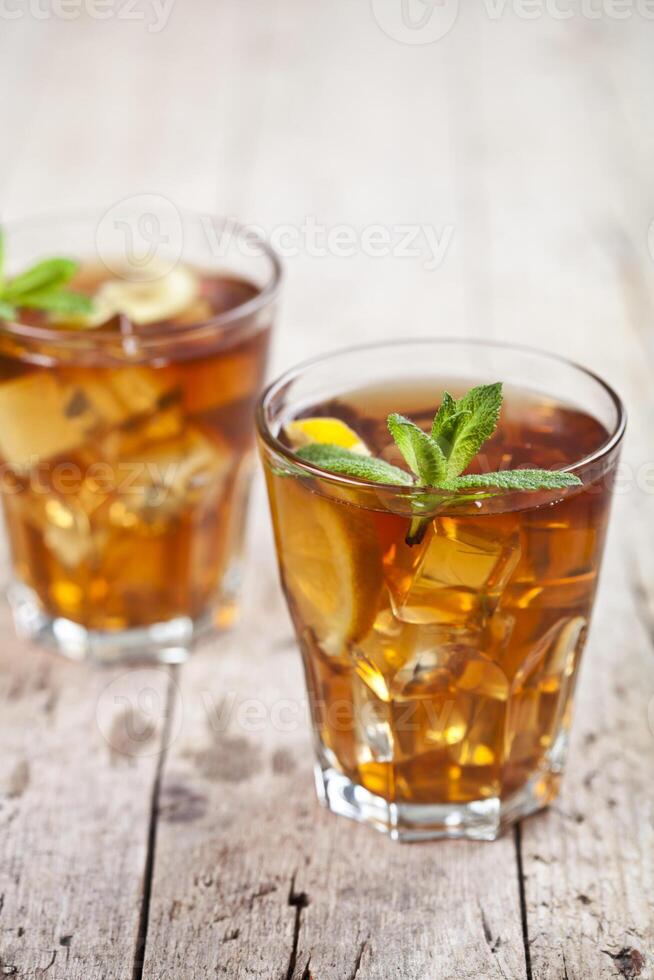 Two glasses with traditional iced tea with lemon, mint leaves and ice cubes in glass on rustic wooden table. photo