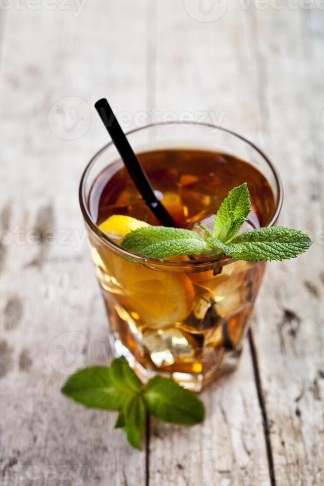 Traditional iced tea with lemon, mint leaves and ice cubes in glass on rustic wooden table photo