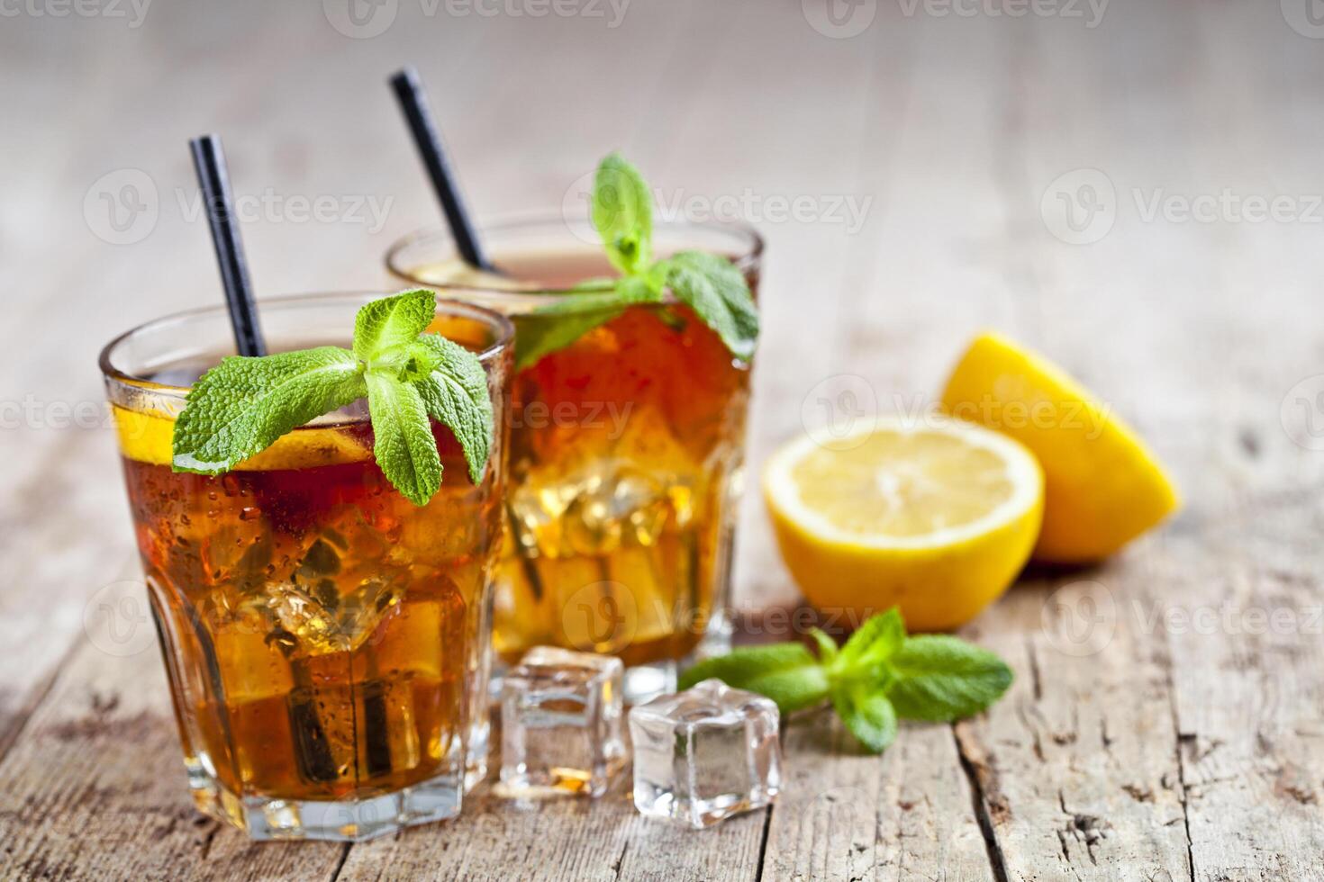 Traditional iced tea with lemon, mint leaves and ice cubes in glasses on rustic wooden table. photo