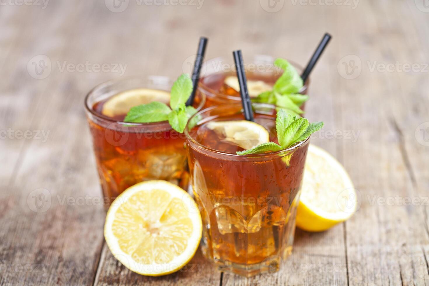 Ttree glasses of traditional iced tea with lemon, mint leaves and ice cubes on rustic wooden table. photo