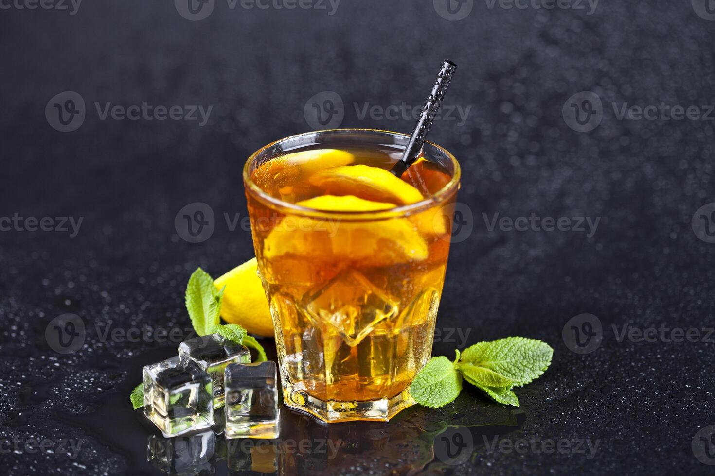 Traditional iced tea with lemon, mint leaves and ice cubes in glass on wet black background. photo