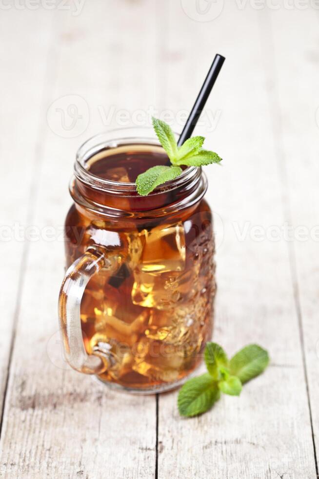 Traditional iced tea with lemon, mint leaves and ice cubes in glass jar on rustic wooden table. photo