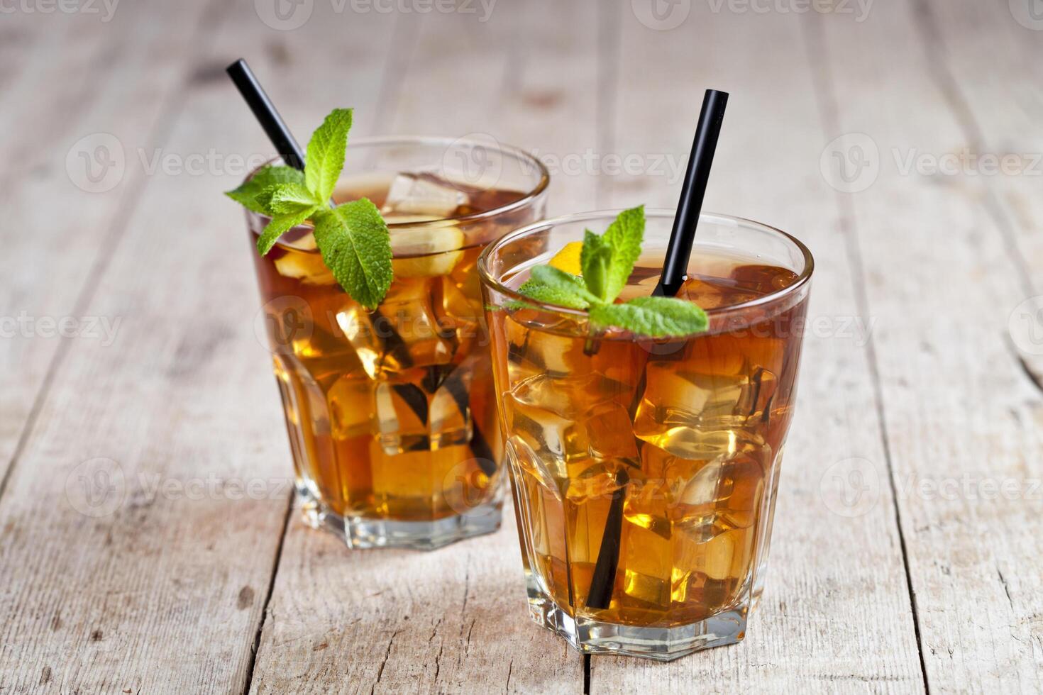 Traditional iced tea with lemon, mint leaves and ice cubes in two glasses on rustic wooden table. photo