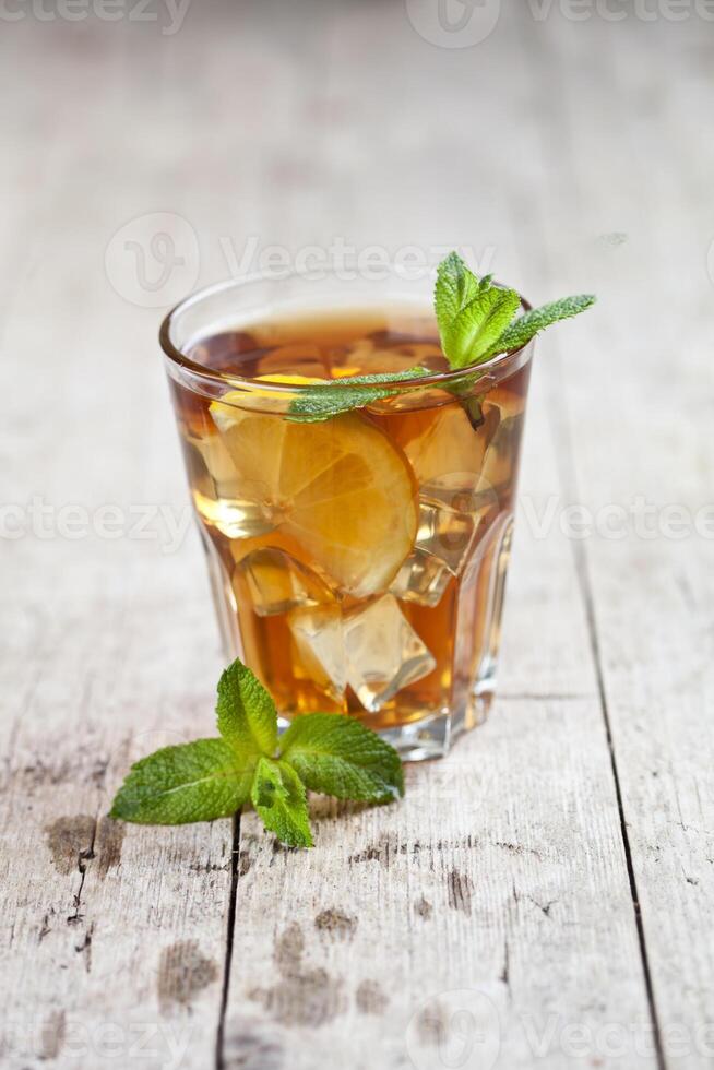 Traditional iced tea with lemon, mint leaves and ice in glass on rustic wooden table. photo