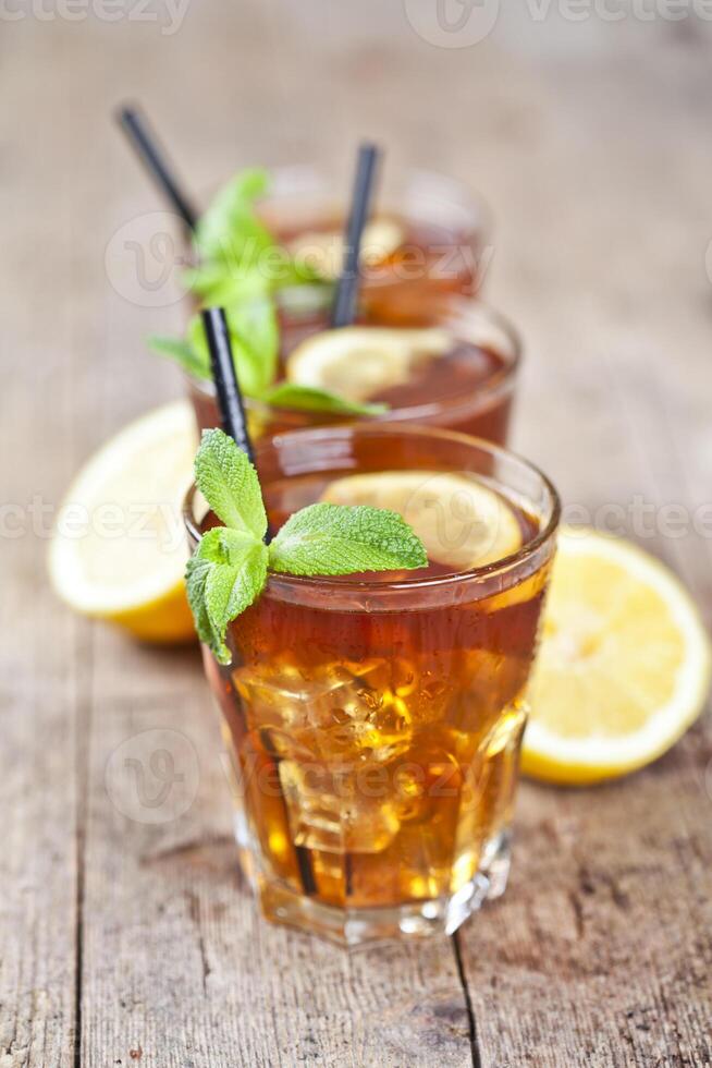 Traditional iced tea with lemon, mint leaves and ice cubes in three glasses on rustic wooden table. photo