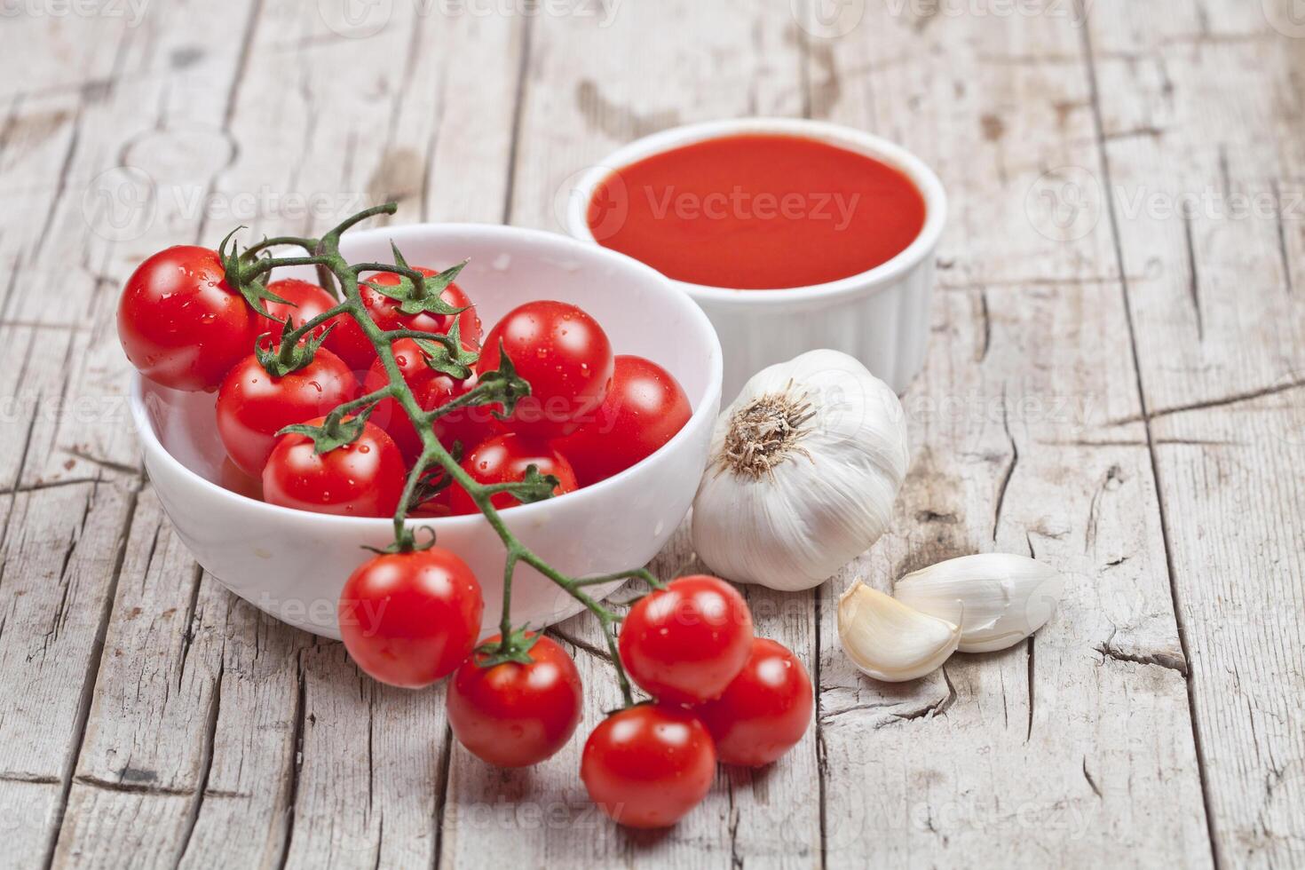 Fresh tomatoes in white bowl, sauce and raw garlic on rustic wooden table. photo