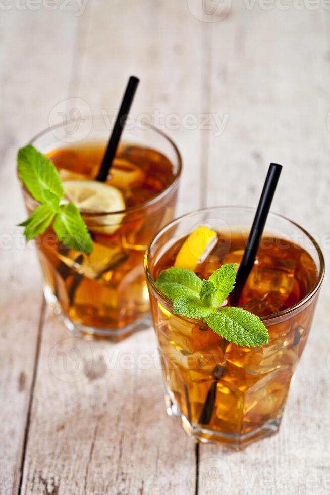 Traditional iced tea with lemon, mint leaves and ice cubes in two glasses on rustic wooden table. photo