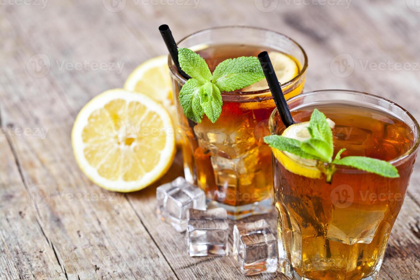 Traditional iced tea with lemon, mint leaves and ice cubes in two glasses on rustic wooden table background. photo