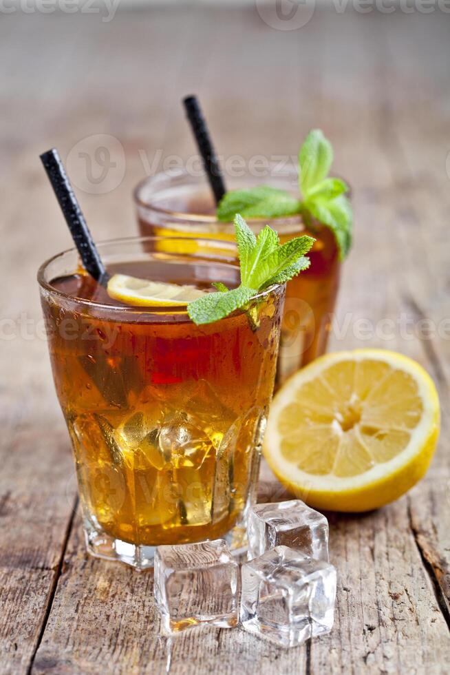 Traditional iced tea with lemon, mint leaves and ice cubes in two glasses on rustic wooden table. photo