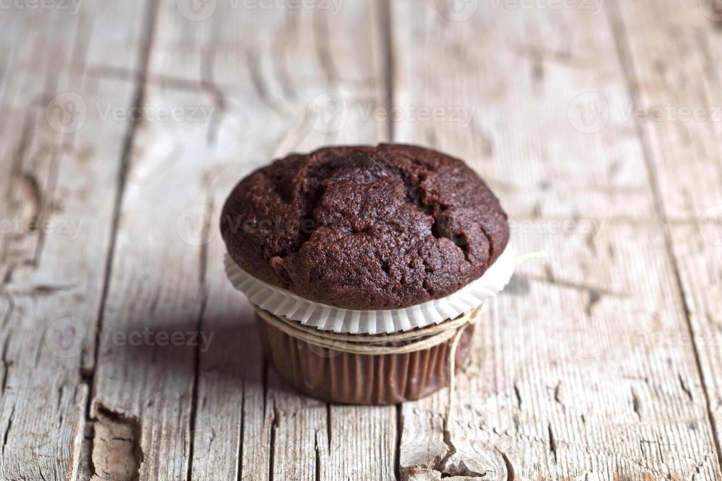 Fresh single dark chocolate muffin on rustic wooden table. photo