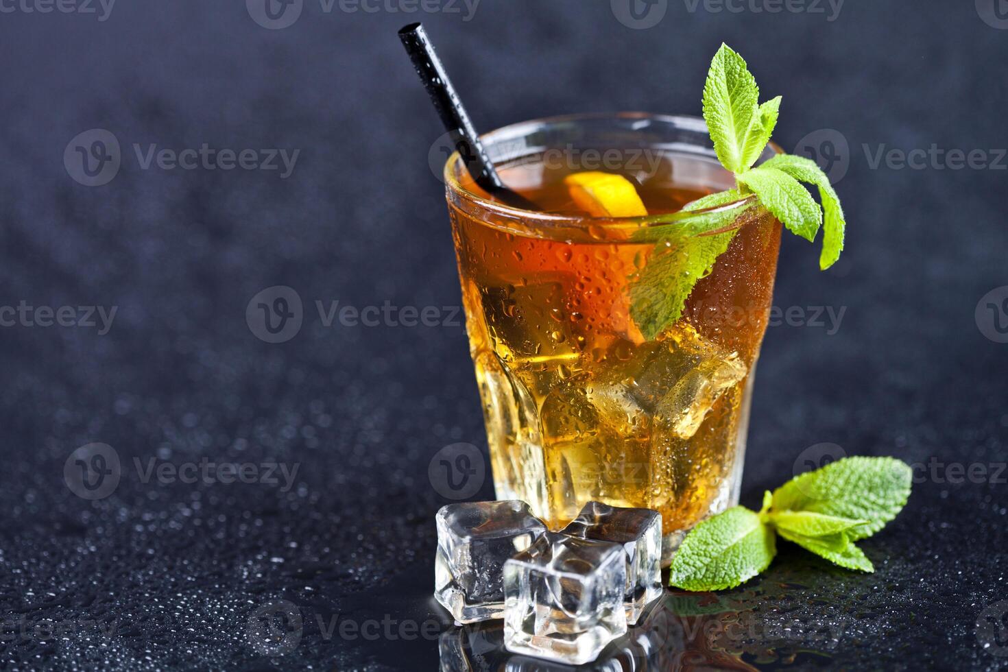 Iced tea with lemon, mint leaves and ice cubes in glass on wet black background. photo