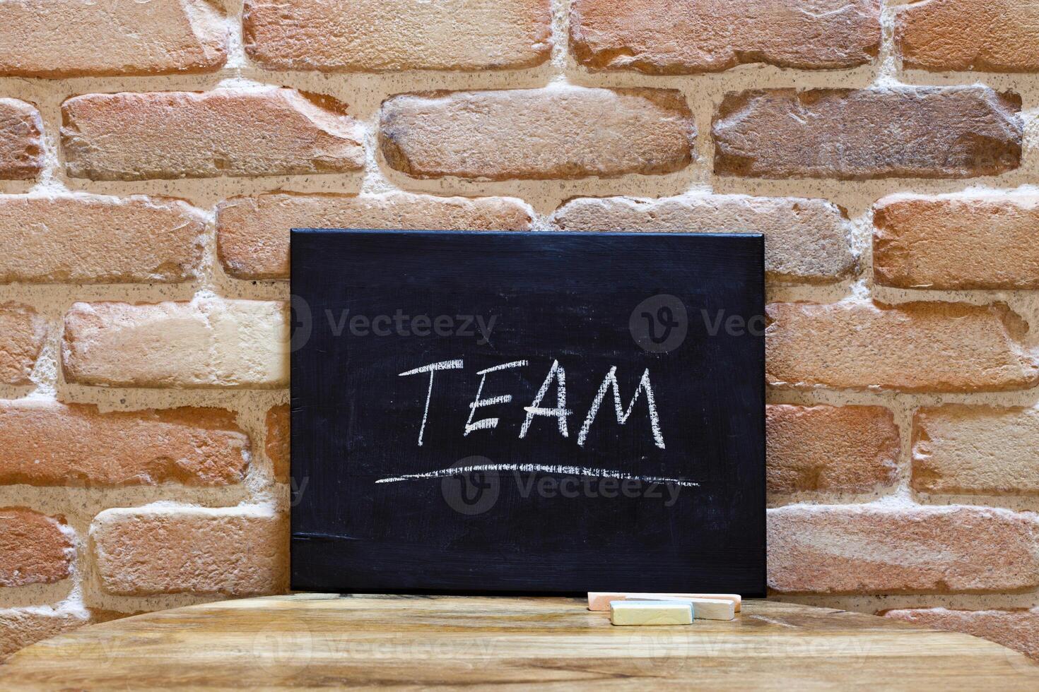 Blackboard with the word Team drown by hand on wooden table on brick wall background. photo