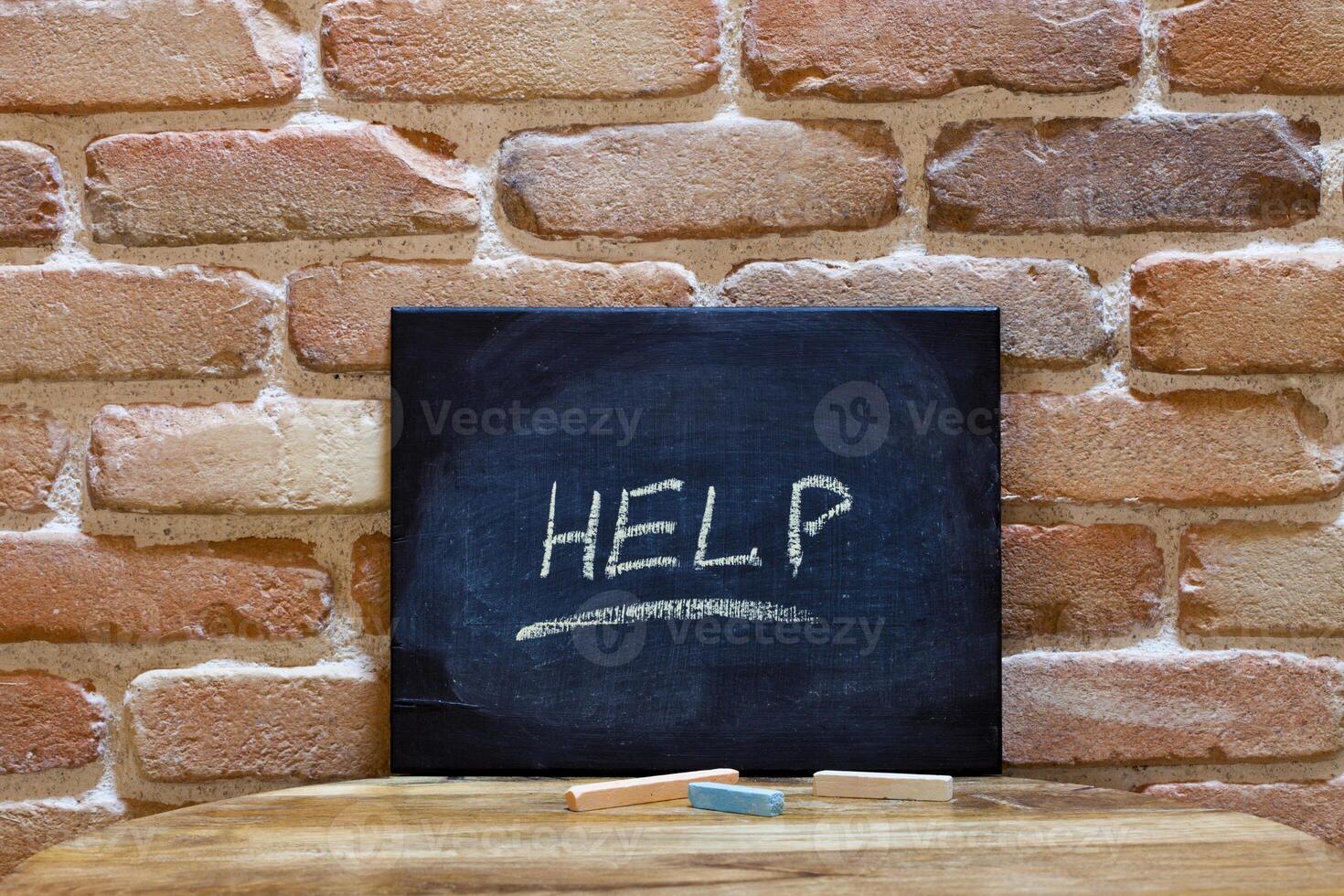 Blackboard with the word Help drown by hand on wooden table on brick wall background. photo