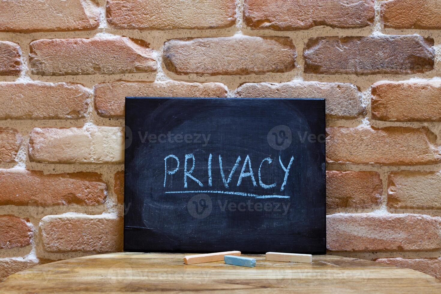Black board with the word Privacy drown by hand on wooden table on brick wall background. photo