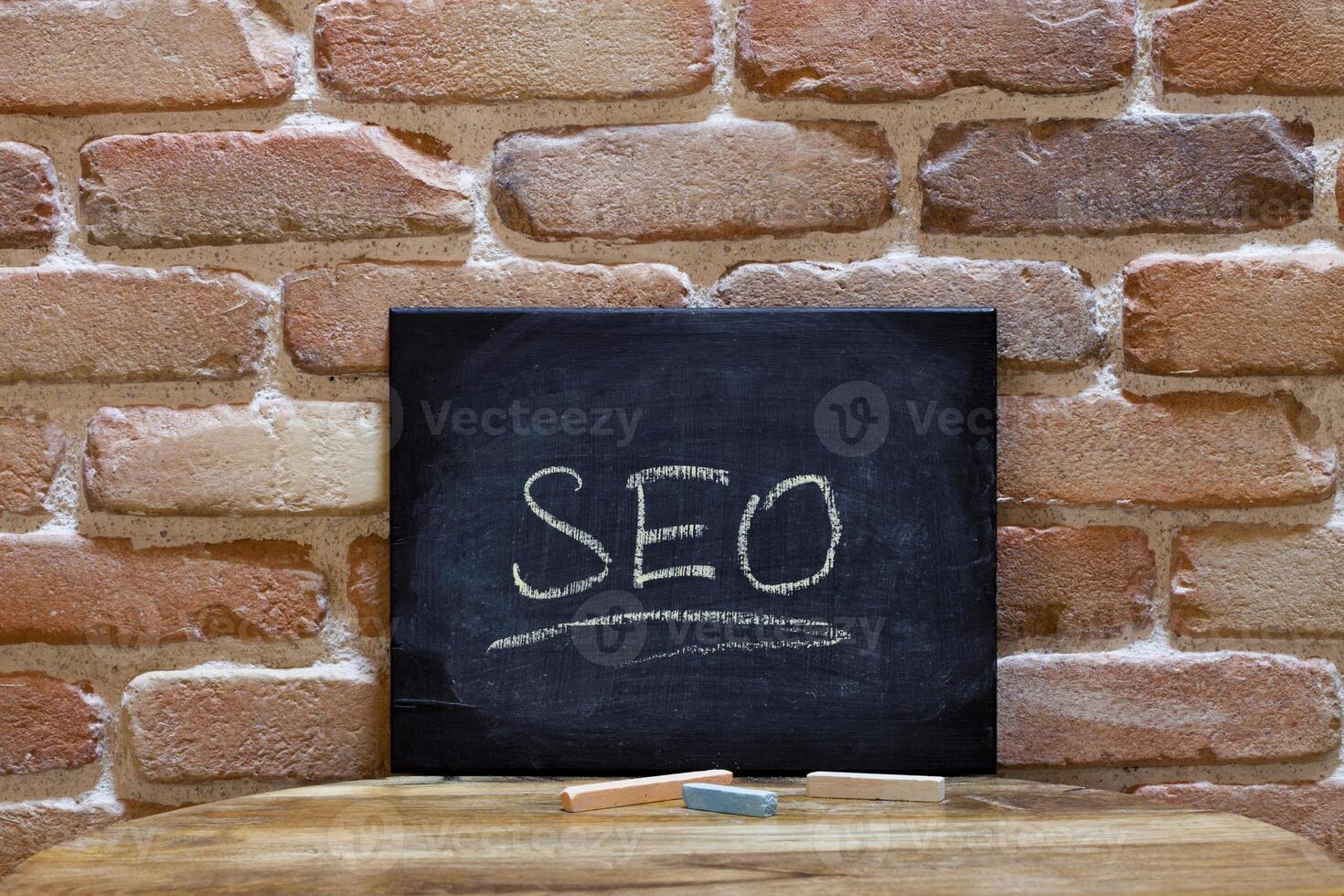 Black board with the word SEO drown by hand on wooden table on brick wall background. photo