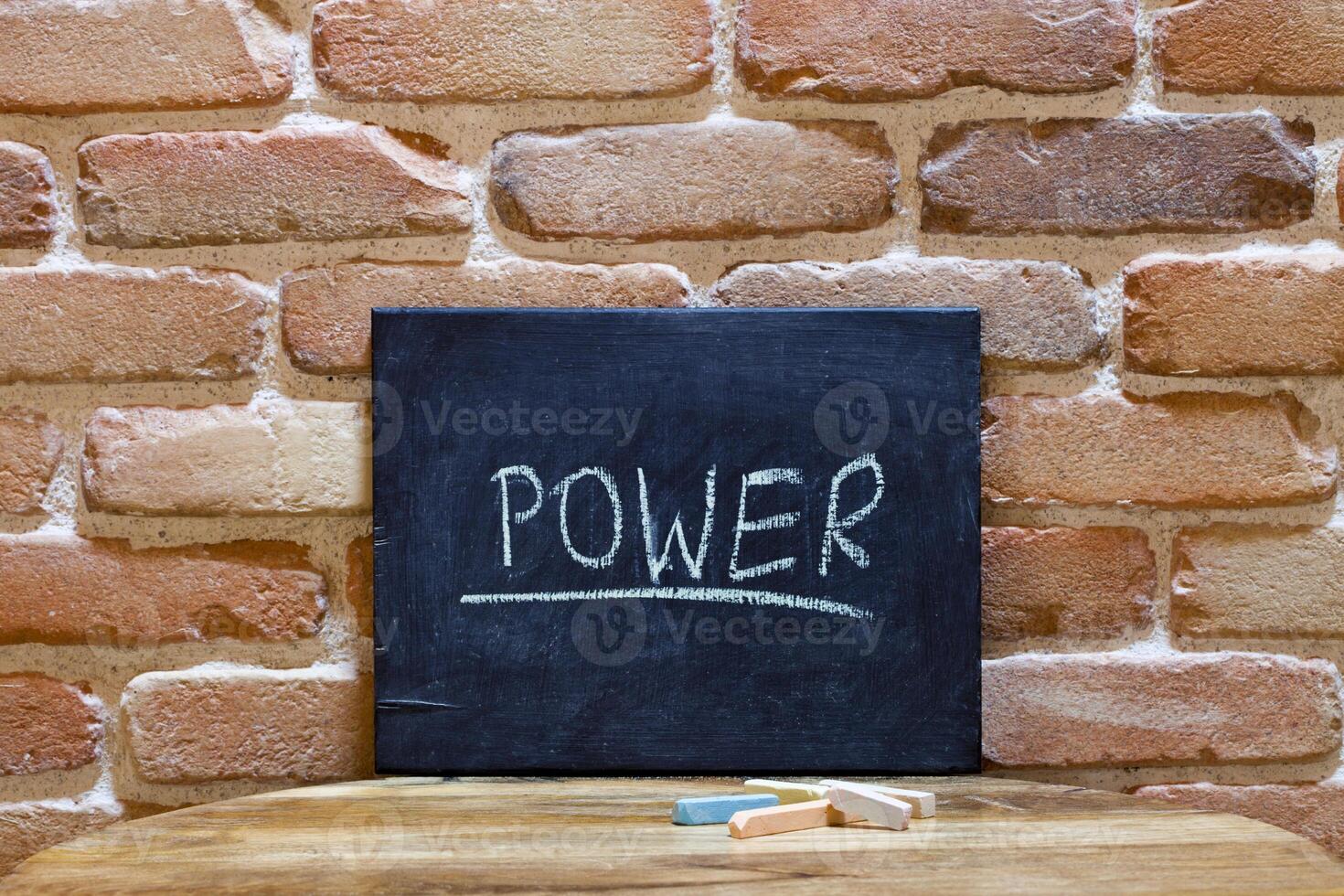 Chalk board with the word Power drown by hand on wooden table on brick wall background. photo