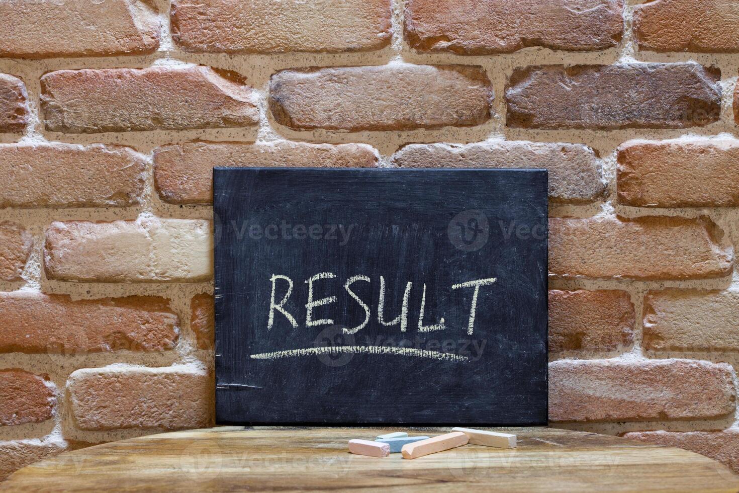 Chalk board with the word RESULT drown by hand on wooden table on brick wall background. photo