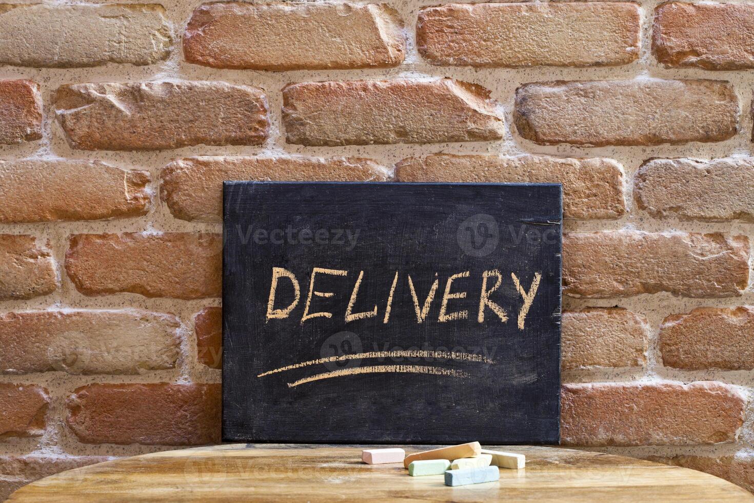 Chalk board with the word DELIVERY drown by hand on wooden table on brick wall background. photo