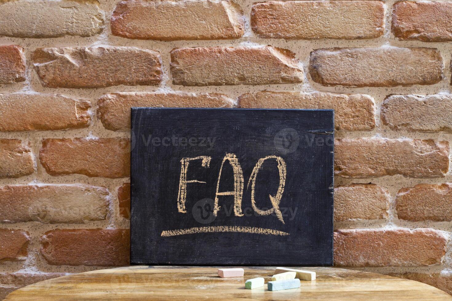 Black board with the word FAQ drown by hand on wooden table on brick wall background. photo