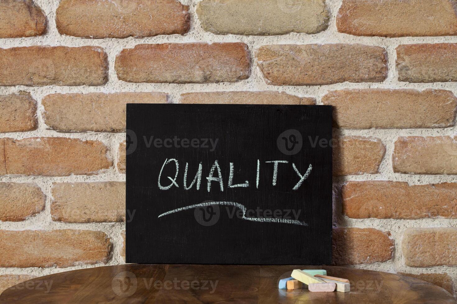 Chalk board with the word QUALITY drown by hand on wooden table on brick wall background. photo