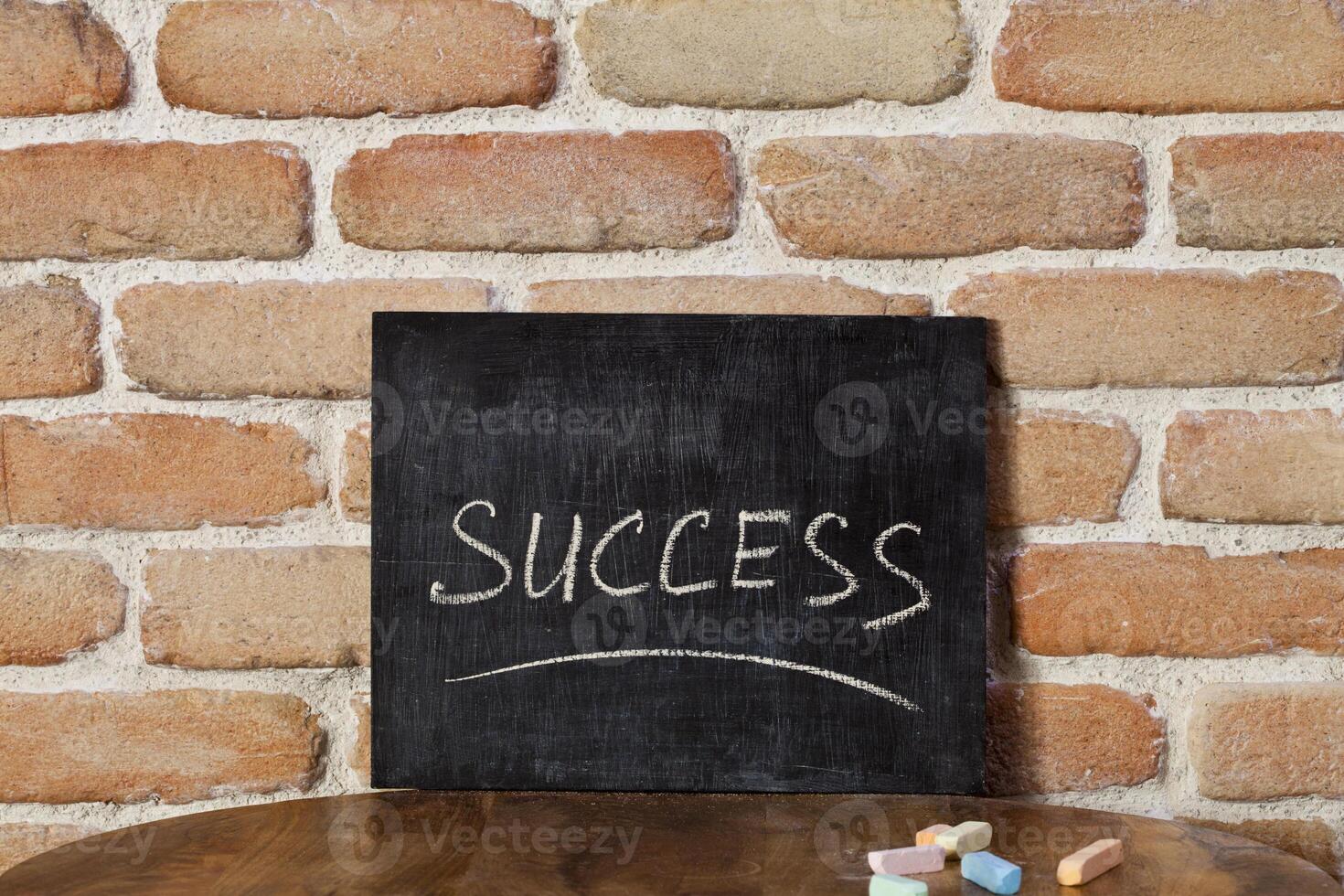 Chalk board with the word SUCCESS drown by hand on wooden table on brick wall background. photo