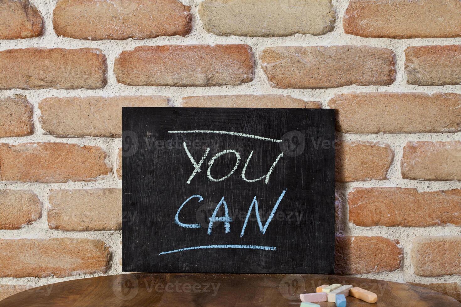 Black board with the phrase YOU CAN drown by hand on wooden table on brick wall background. photo