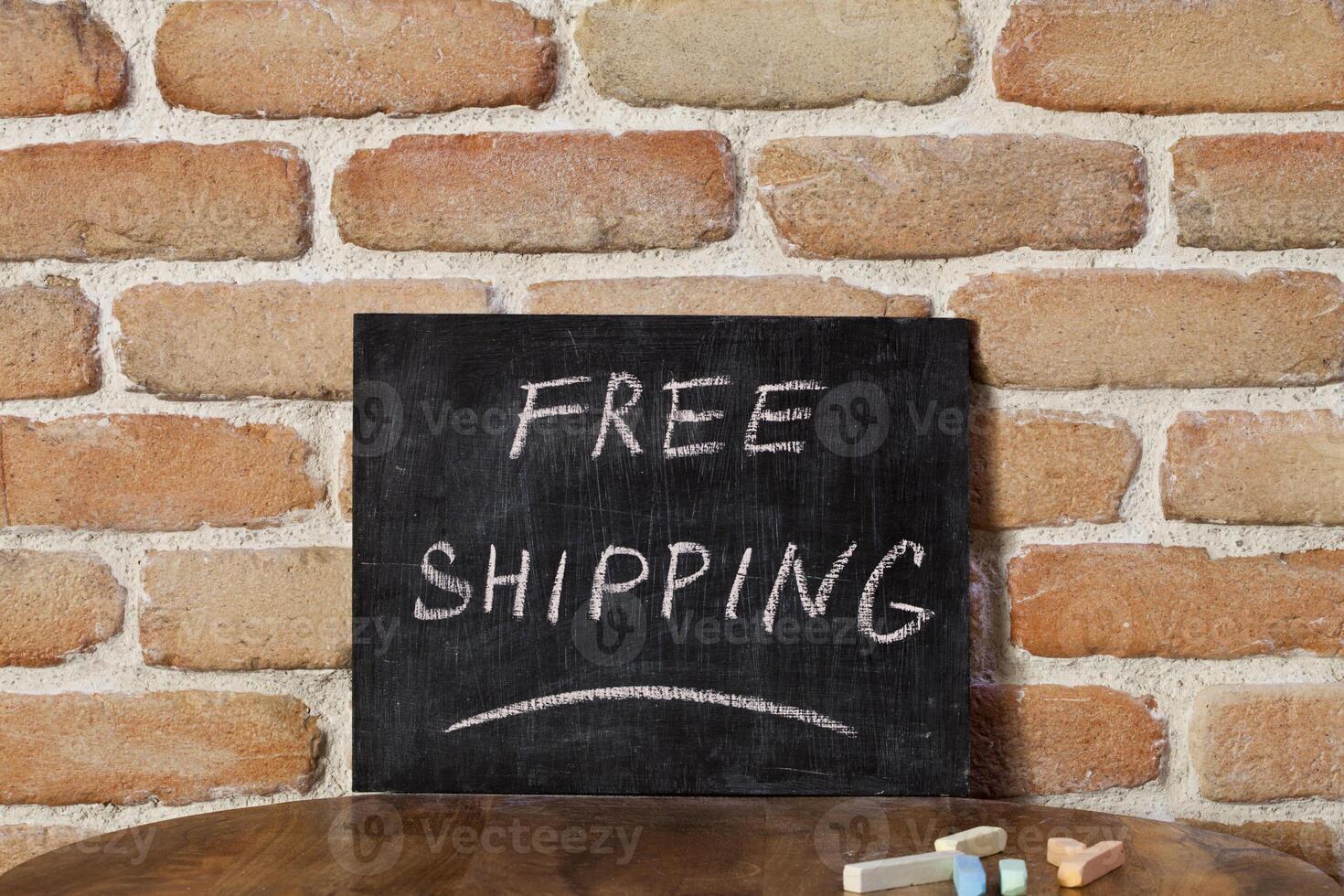 Black chalkboard with the phrase FREE SHIPPING drown by hand on wooden table on brick wall background. photo