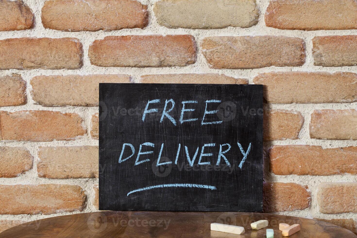 Black chalkboard with the phrase FREE DELIVERY drown by hand on wooden table on brick wall background. photo