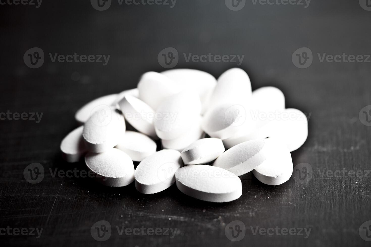 Pile of white drug pills laying on black board background. photo