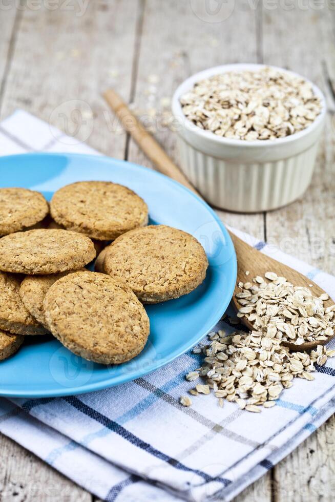 Fresh baked oat cookies on blue ceramic plate on linen napkin and oak flakes on rustic wooden table. photo
