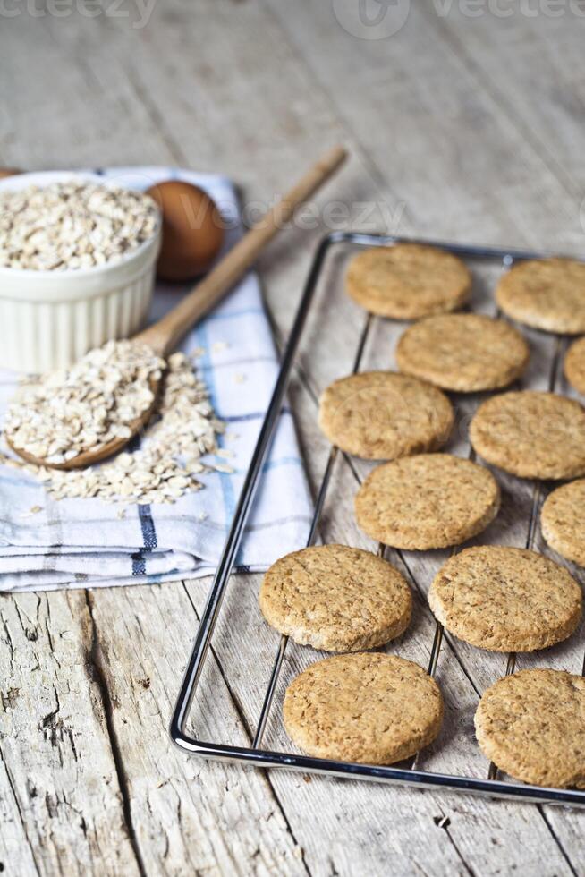 Baking grid with fresh oat cookies on rustic wooden table background, ingredients and kitchen utensil. photo