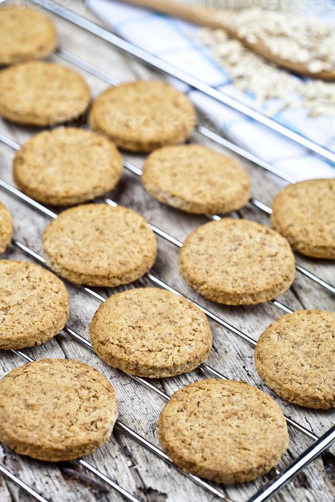 Baking grid with fresh oat cookies on rustic wooden table background, ingredients and kitchen utensil photo