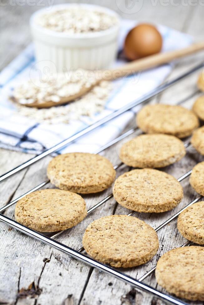 Baking grid with fresh oat cookies on rustic wooden table background, ingredients and kitchen utensil closeup. photo