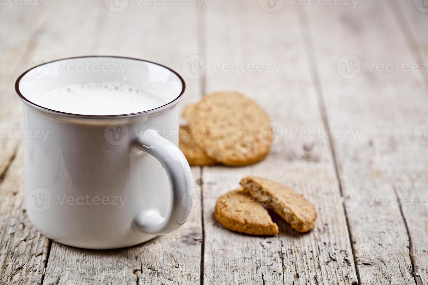 Cup of milk and some fresh baked oat cookies on rustic wooden table background. photo