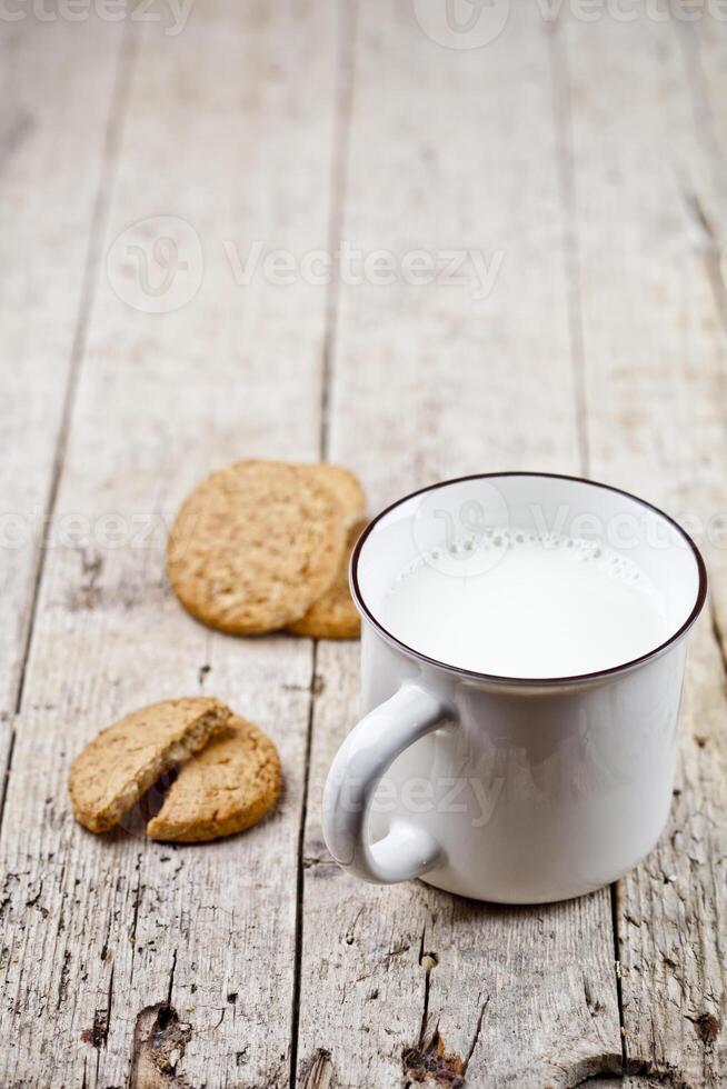 Cup of milk and some fresh baked oat cookies on rustic wooden table background. photo